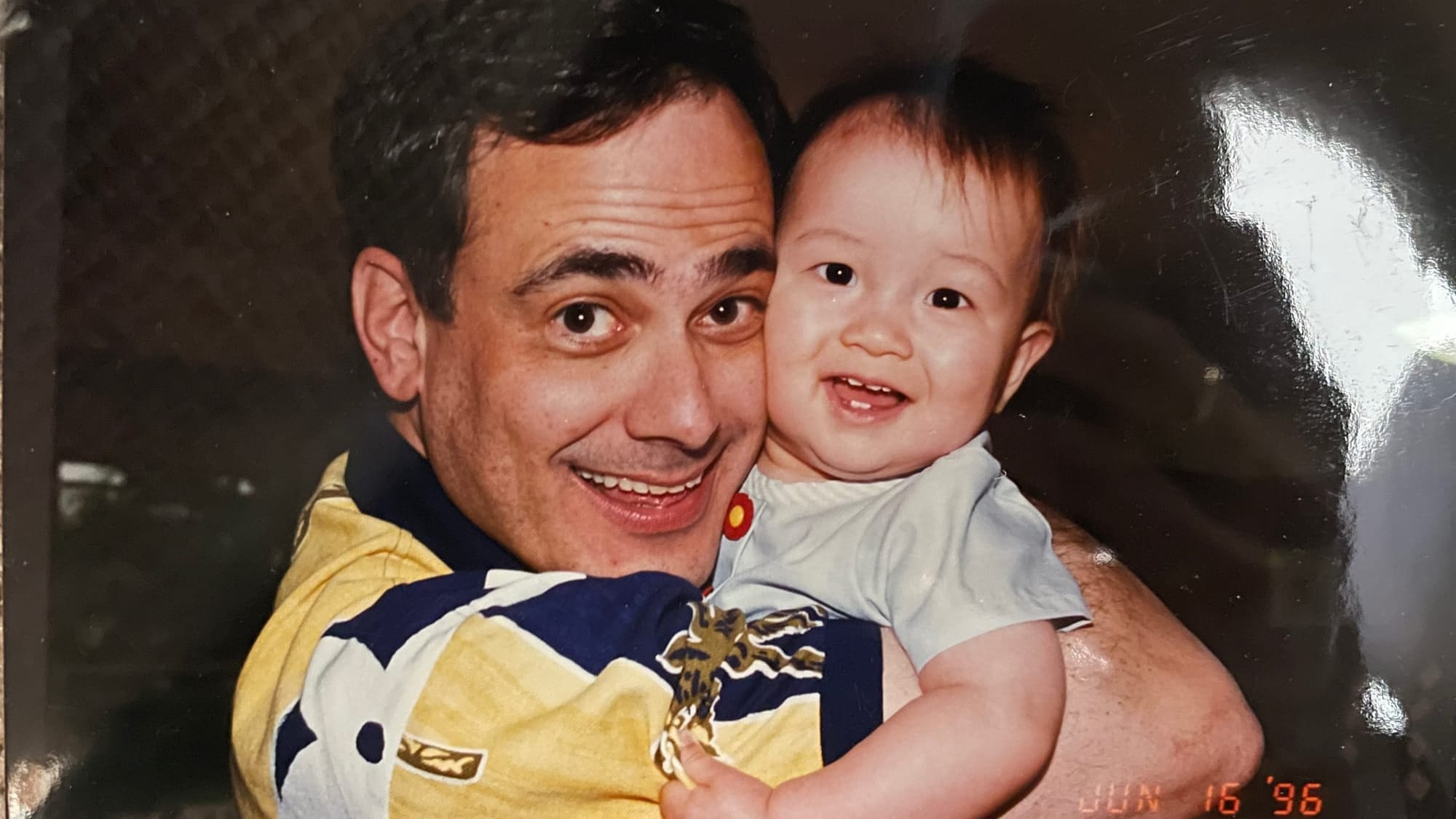 A man holds a baby, both of whom are smiling.