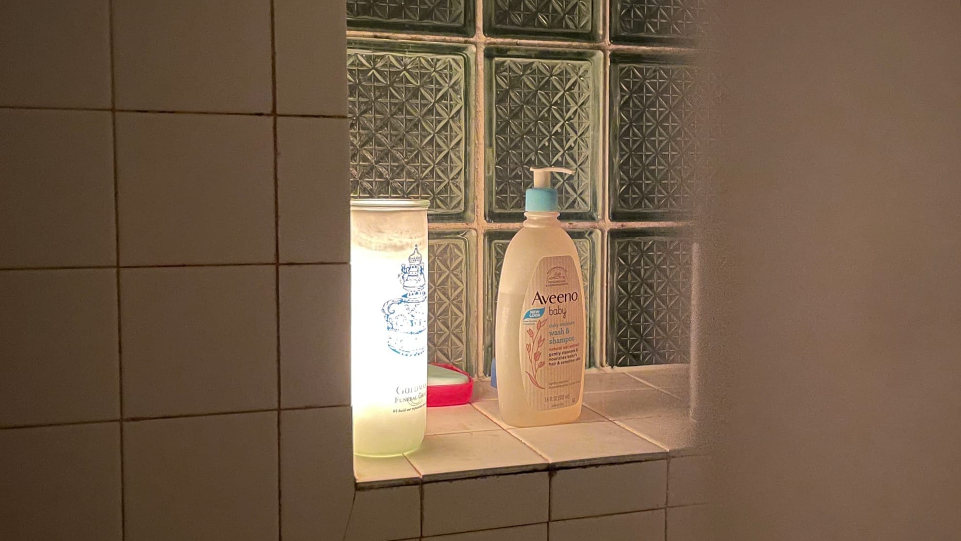 A large candle next to Aveeno soap in a bathroom.