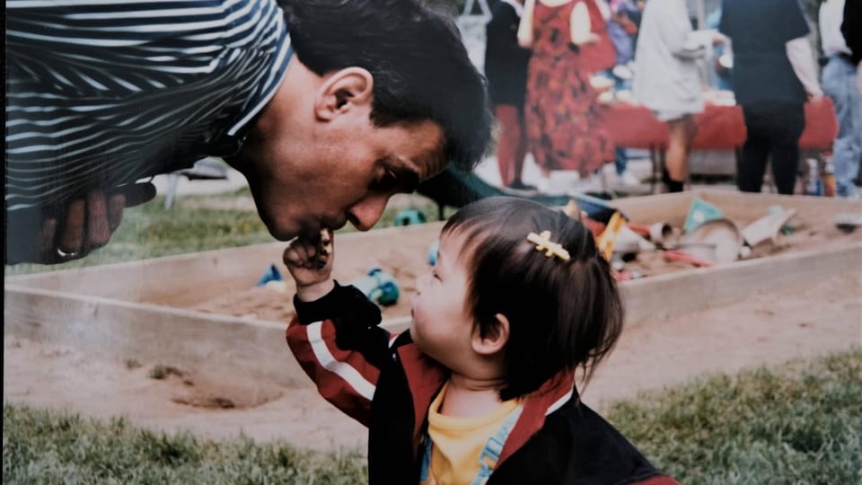 A man bends down as his kiddo reaches for his lips.